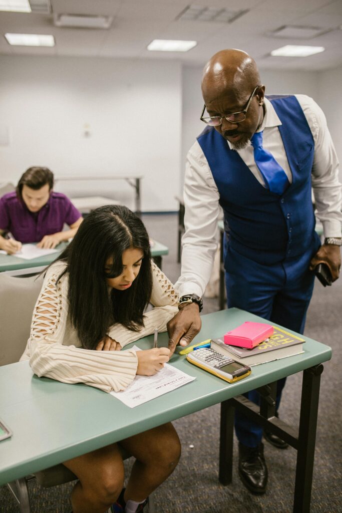 pexels-photo-7092538-7092538 Educator assisting student during an exam in a classroom setting, emphasizing support in education.